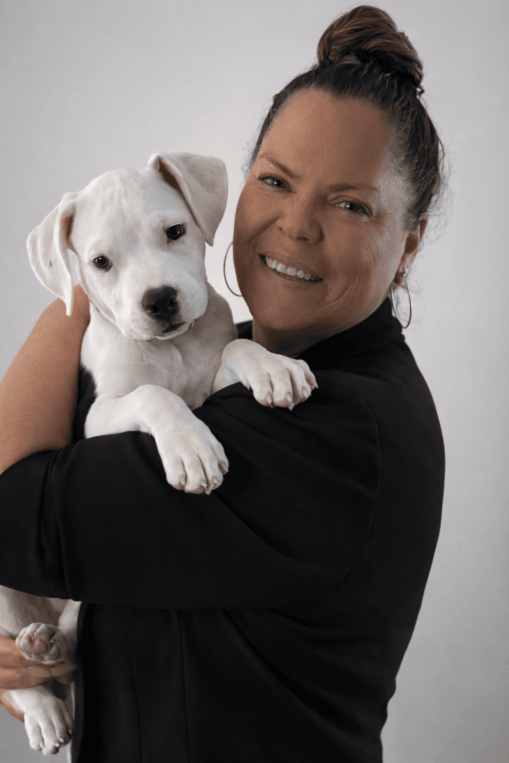 Claudia Altman, founder of Forever Kuddles Fosters, smiling while holding a small white puppy in a studio portrait